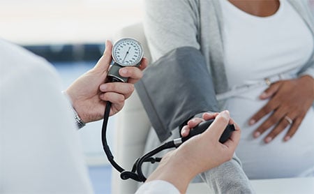 Healthcare professional measuring pregnant patient's blood pressure with a sphygmomanometer.