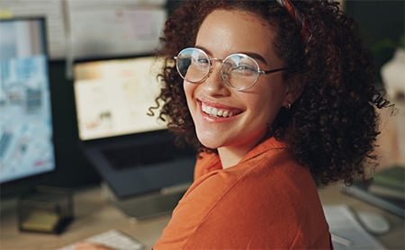 A woman smiles at the camera while seated at her desk